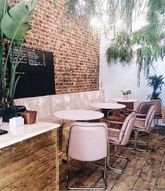 the interior of a restaurant with pink chairs and wooden tables in front of a brick wall