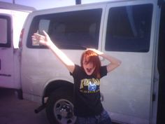 a woman standing in front of a white van with her arms up and hands behind her head