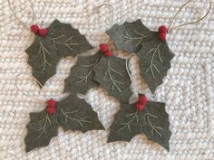 four felt holly leaves with red berries on them sitting on a white cloth covered surface