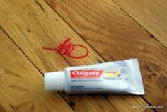 a tube of toothpaste sitting on top of a wooden floor next to a red string