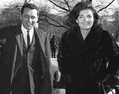 an old black and white photo of a man and woman walking in front of trees