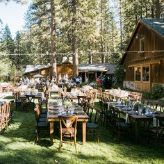 tables and chairs are set up outside in the grass near wooden buildings with string lights strung from them