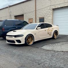 a white car with gold wheels parked in front of a brick building next to other cars