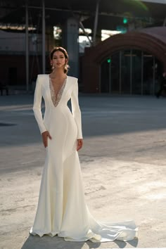 a woman in a long sleeved white dress posing for the camera with her hands on her hips