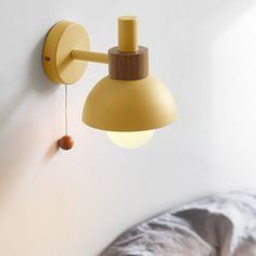 a yellow wall light hanging from the side of a white wall next to a bed