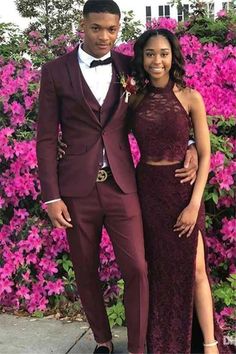 a man and woman standing next to each other in front of purple flowers wearing tuxedos