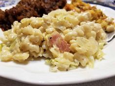 a white plate topped with macaroni and cheese covered in sauce next to meat