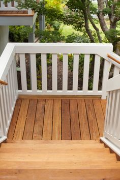 a wooden deck with white railings and wood flooring in front of some trees