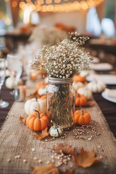 the table is set with pumpkins, baby's breath and flowers in a mason jar