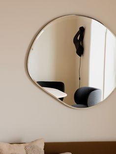 a round mirror hanging on the wall above a bed with a black chair in front of it