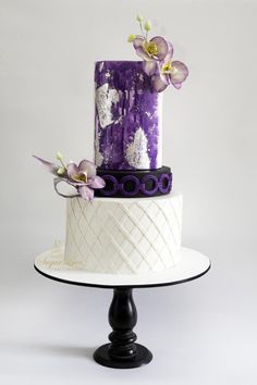 a three tiered cake with purple and white frosting, decorated with orchids