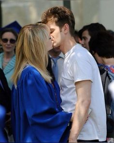 a man and woman kissing each other in front of a group of people wearing graduation gowns