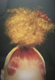 the back of a woman's head with red and yellow hair on top of it