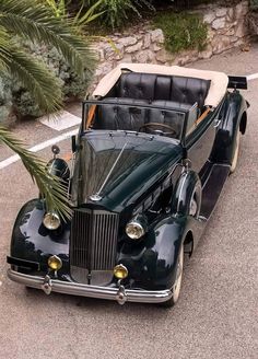 an old fashioned car parked on the side of the road next to a palm tree