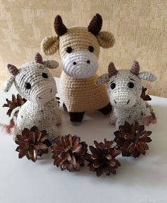 three small crocheted animals sitting next to each other on a table with pine cones