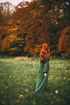 a woman with red hair is standing in the grass and looking up into the sky