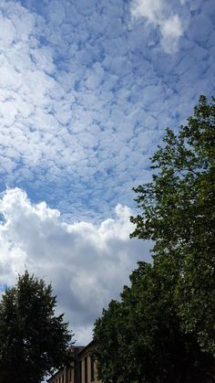 the sky is full of clouds and some trees are in front of it on a sunny day