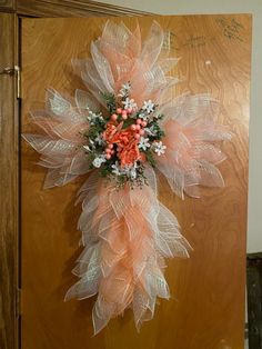 an orange and white wreath hanging on a wooden door with flowers in it's center