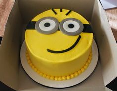 a yellow cake decorated like a minion with googly eyes in a cardboard box