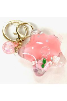 a pink keychain with a star shaped object on it's side and two other items in the background