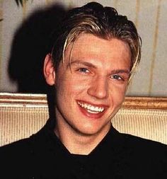 a close up of a person wearing a black shirt and smiling at the camera with one eye open