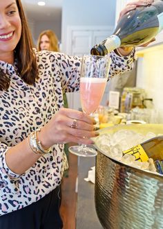 a woman pouring champagne into a glass in front of a pot full of ice cubes