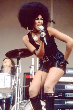 a woman in short shorts and boots holding a microphone while standing next to a drum set