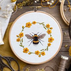 a cross stitch bee with yellow flowers in the hoop on a wooden table next to scissors and thread