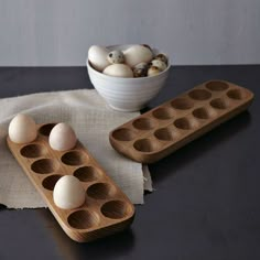 two wooden trays filled with eggs sitting on top of a table next to a bowl