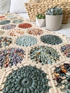 a crocheted blanket on a bed next to a basket with succulents