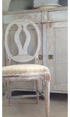 an old white chair sitting in front of a cabinet with a vase on top of it