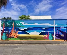 a large mural on the side of a building in front of a blue sky and ocean