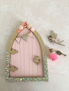 a pink fairy door with flowers on it and some other items around the perimeters