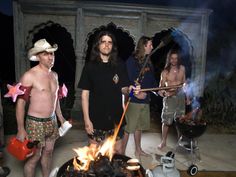 several men standing around a fire pit with one holding a stick