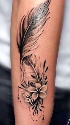 a black and white photo of a feather with flowers on the side of a woman's leg