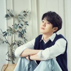 a young man sitting on the floor in front of a plant