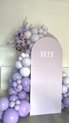 balloon arch with white and purple balloons in front of it that says beth on the side