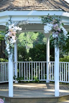 a gazebo with flowers and greenery on the top is surrounded by white railings