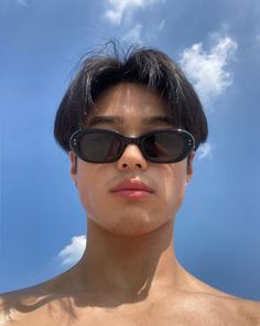 a shirtless man wearing sunglasses under a blue sky with clouds in the back ground