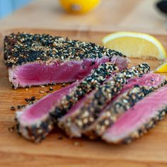 a piece of meat with sesame seeds and lemon wedges next to it on a cutting board