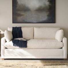 a white couch with a blanket on it in front of a painting