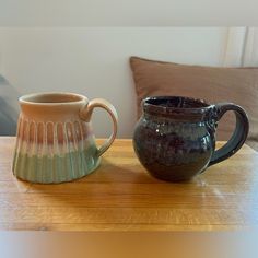 two coffee mugs sitting on top of a wooden table next to eachother