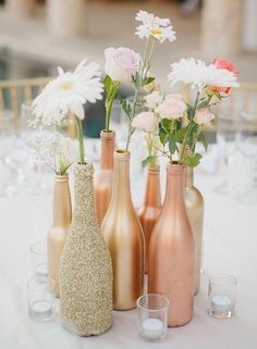 three vases filled with flowers sitting on top of a white table covered in glasses