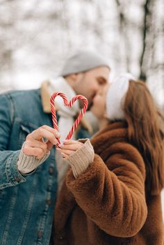 a man and woman kissing while holding a candy cane in front of their face,