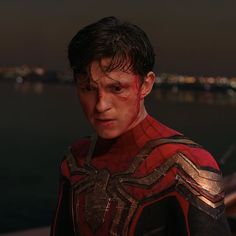 a young man dressed as spider - man stands in front of the water at night