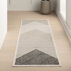 a white and black rug on the floor next to a potted plant in a room