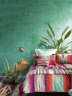 a bedroom with green brick wall and colorful bedding, potted plant on nightstand