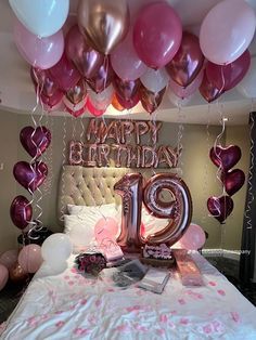 a bed with pink and white balloons on top of it, next to a large number 19 sign