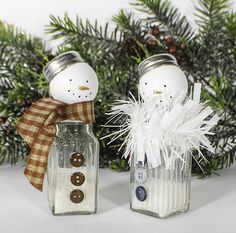 two salt shakers sitting next to each other with snowmen on them and pine branches in the background