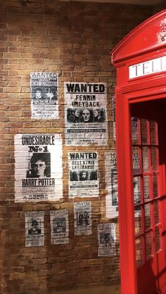 a red phone booth sitting in front of a brick wall with posters on the wall